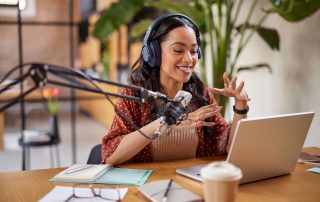Eine Frau sitzt mit Kopfhörern und Mikrofon vor einem Laptop und nimmt einen Podcast auf.