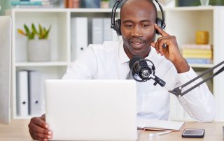 Ein Mann sitzt mit einem Mikrofon vor einem Laptop und nimmt einen Podcast auf.