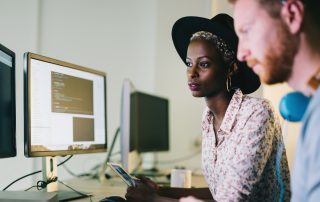 Eine Frau und ein Mann programmieren einen gemeinsamen Code an einem Computer.