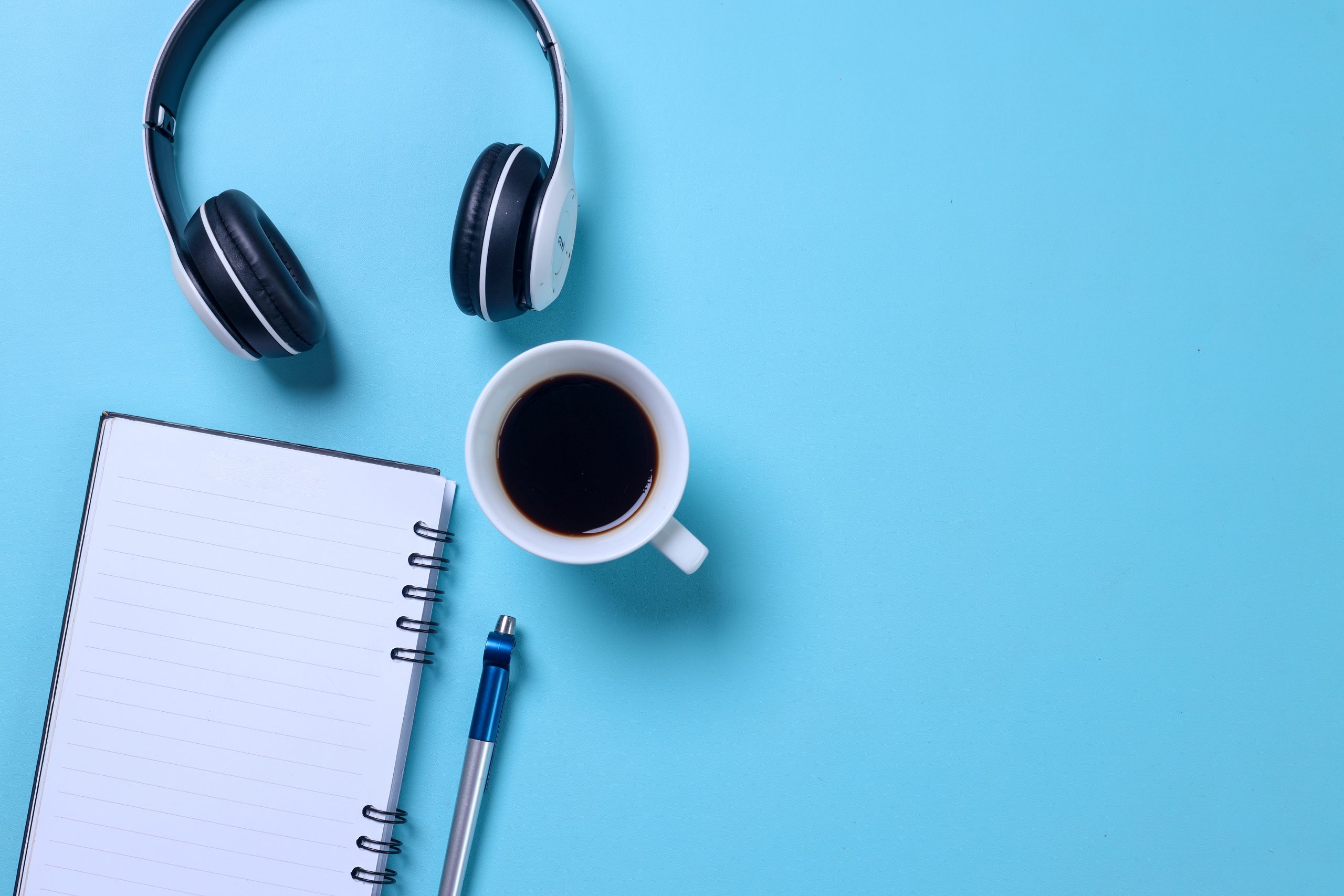 Kopfhörer, Kaffee und ein Notizblock auf einem blauen Hintergrund.